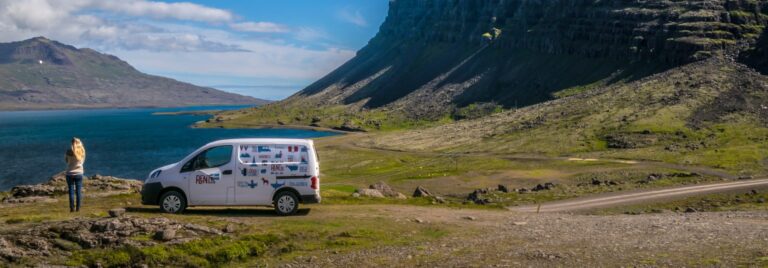 rent.is camper parked in a green fjord next to a woman overlooking the sea